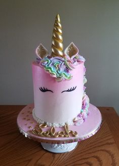 a pink cake with a unicorn's face on top and gold trimmings