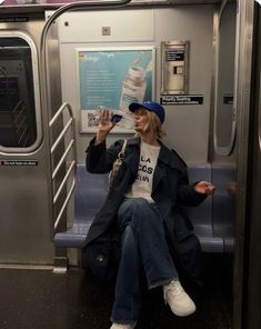 a woman sitting on a subway train with her hand up to her mouth and wearing a hat