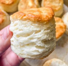 a person holding up a biscuit in front of some other biscuits on a baking sheet