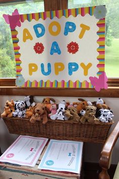 there are stuffed animals in a basket on the table next to two cards and a sign that says adopt a puppy