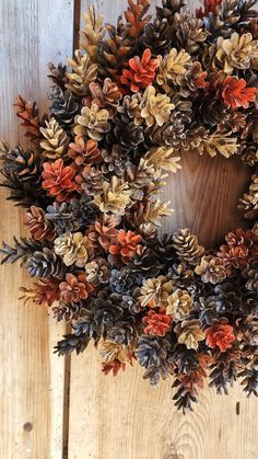 a wreath made out of pine cones on a wooden door with red and green leaves