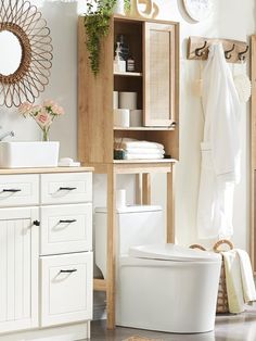 a white toilet sitting in a bathroom next to a wooden cabinet and sink with towels hanging on it