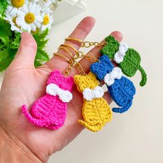 small crocheted keychains are being held by someone's hand with flowers in the background