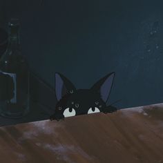 a black cat peeking out from behind a wooden table with a bottle on the side