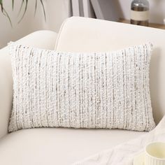 a white pillow sitting on top of a couch next to a cup and saucer