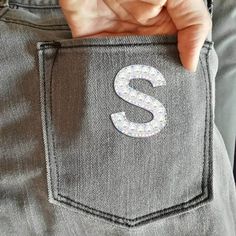 someone is holding their pocket with the letter s on it's side and there is a small sequin - embellishment in the pocket