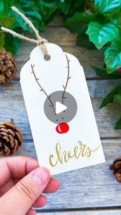 a hand holding a christmas gift tag with the word cheers on it and reindeer's nose