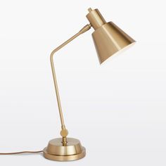 a gold desk lamp on a white surface with a cord attached to the end of it