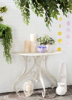 a white table with candles and flowers on it next to a brick wall in front of a potted plant