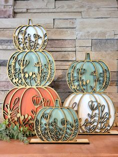 three decorative pumpkins sitting on top of a wooden table next to a brick wall