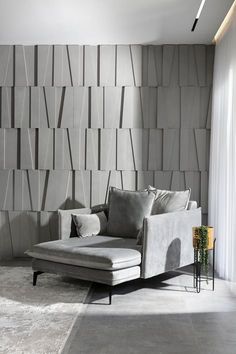 a couch sitting in front of a wall covered in grey tiles and pillows on top of a rug