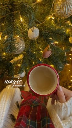 a person holding a cup of coffee in front of a christmas tree with ornaments on it