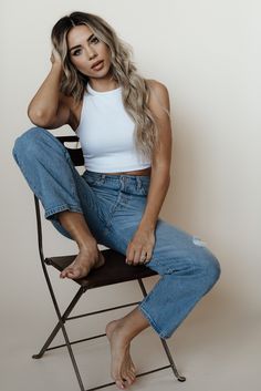 a woman sitting in a chair with her legs crossed and looking at the camera while wearing ripped jeans