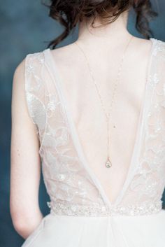 the back of a woman's wedding dress with a necklace on her left shoulder