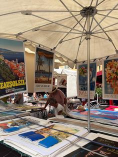 there is a man sitting under an umbrella at the book sale with many books on it