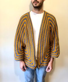 a man standing in front of a wall wearing a yellow and blue knitted cardigan