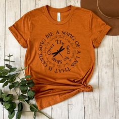 an orange t - shirt with the words sing me a song on it next to a hat