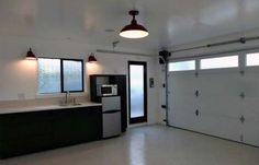 an empty kitchen with a refrigerator and microwave in it's center area, next to a garage door