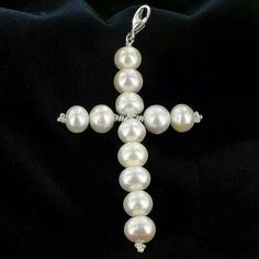 a cross made out of white pearls on a black cloth with a chain attached to it