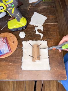 a person is using scissors to cut paper on a piece of wood that has been placed on the table