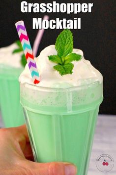 there is a hand holding a green drink with whipped cream and mint on the top