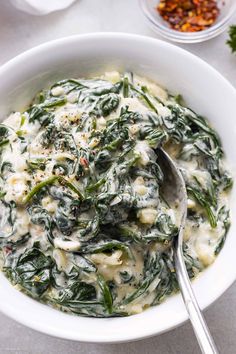 a white bowl filled with spinach and cheese on top of a table next to other dishes