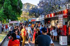 many people are lined up to get food from the trucks at an outdoor event in front of mountains