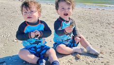 two young boys sitting on the beach eating food