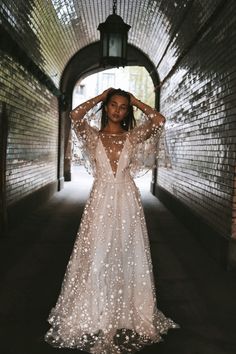 a woman in a long white dress standing in a tunnel with her hands on her head