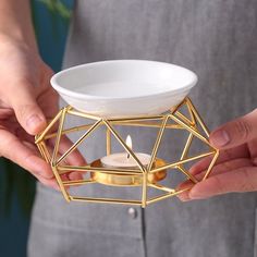 a person holding a small candle holder with a white bowl in it and two hands