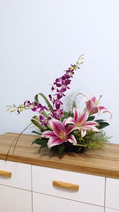 a bouquet of flowers sitting on top of a wooden table next to white drawers and cupboards