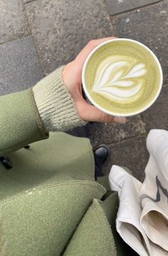 a person holding a cup of matcha latte in their hand on the sidewalk