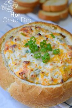 a hot crab dip in a bread bowl with green onions on the side and crackers around it