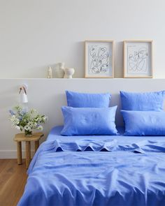 a bed with blue sheets and pillows in a white room next to two pictures on the wall