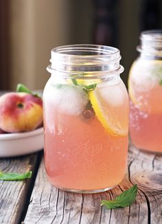 two mason jars filled with pink lemonade, mint and fresh peaches on a wooden table