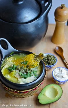 a bowl filled with soup next to two spoons and an avocado