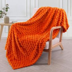 an orange knitted blanket sitting on top of a chair next to a wooden table