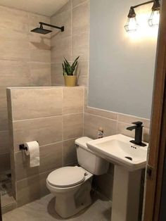 a white toilet sitting next to a sink in a bathroom under a light fixture on a wall