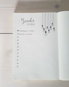 an open notebook with the words books to read written on it and hanging from strings