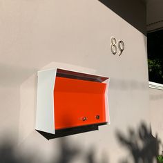 an orange and white mailbox mounted to the side of a building with numbers on it