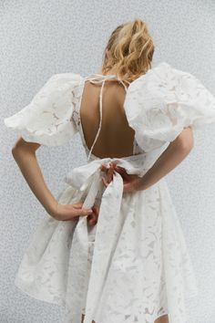 the back of a woman wearing a white dress with an open neck and ruffled sleeves