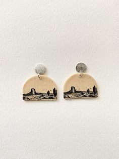 two earrings with skylines on them sitting on top of a white surface next to each other