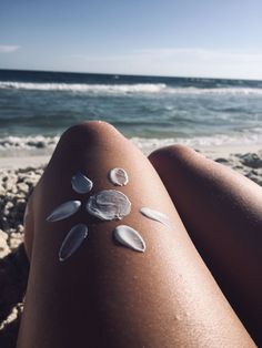 a woman's legs covered in white sand with shells on them and the ocean in the background