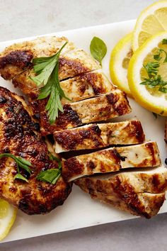 grilled chicken with herbs and lemons on a white platter next to sliced lemons