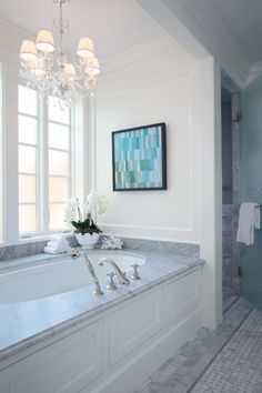 a bathroom with a chandelier and marble counter tops in front of a large bathtub