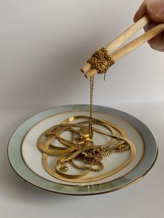 a person holding chopsticks over a plate with gold jewelry on it