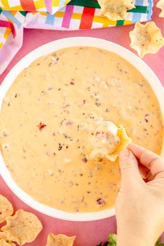 a person dipping tortilla chips into a bowl of quesadilla dip