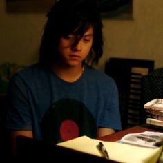 a young man sitting at a table in front of a stack of books