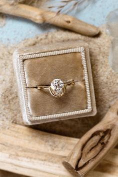 an engagement ring with a diamond sits in a velvet box on top of driftwood