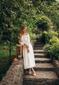 a woman in a white dress is sitting on some steps and smiling at the camera